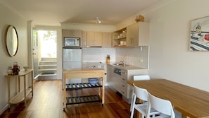 Une cuisine de taille réduite avec une table en bois, des chaises blanches et un four encastré.