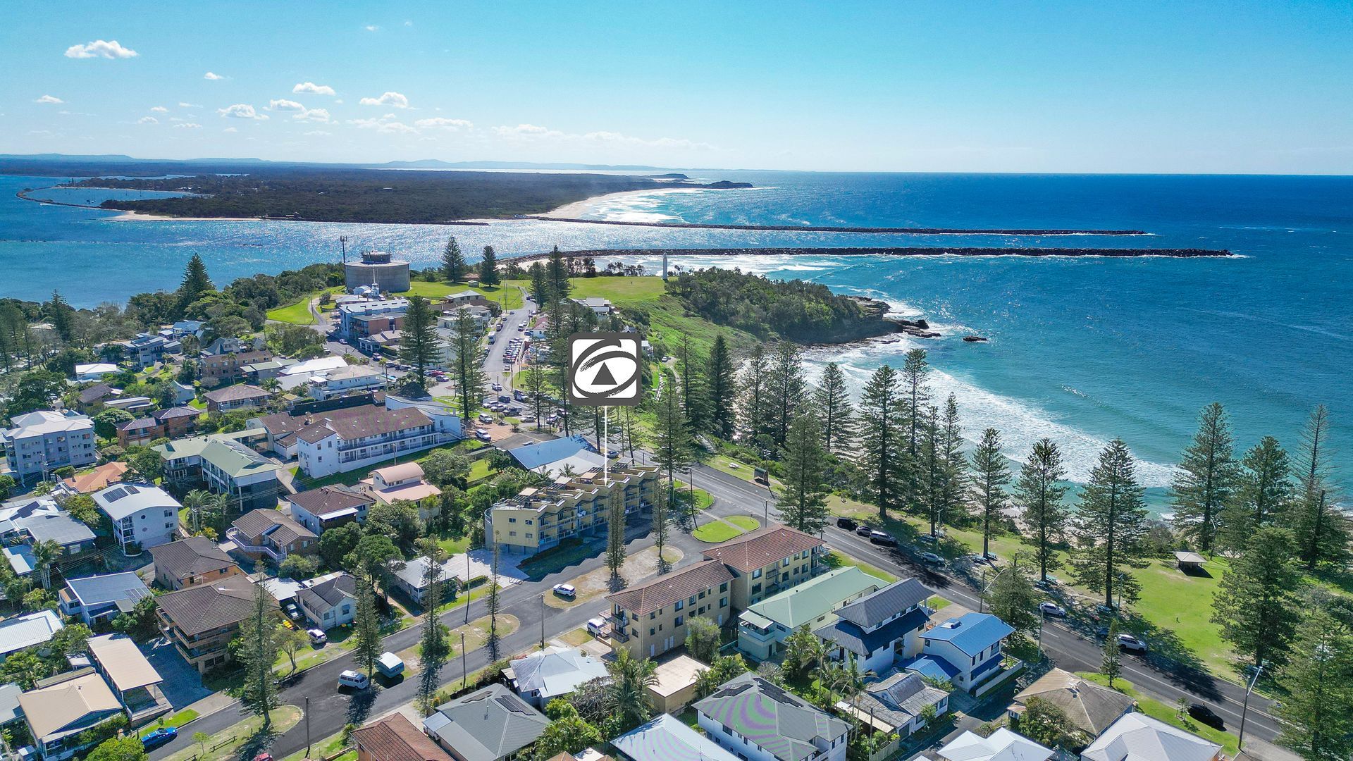 An aerial view of a coastal residential area with houses, a road, and a beach.