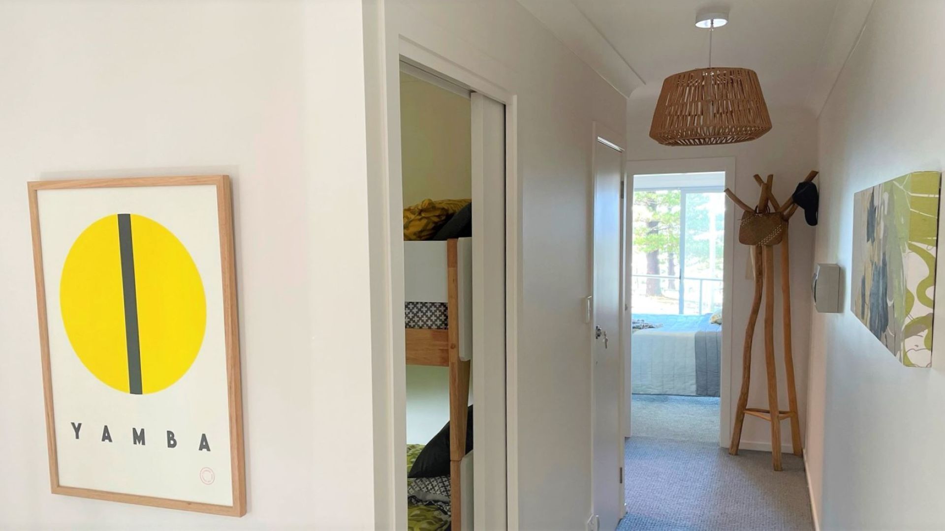 A hallway with a framed artwork, a door leading to a room with a bed, and a hanging coat rack.