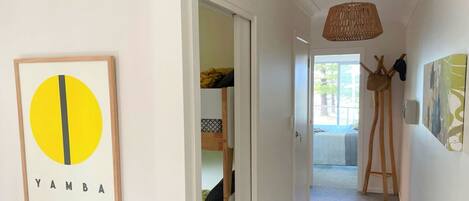 A hallway with a framed artwork, a door leading to a room with a bed, and a hanging coat rack.