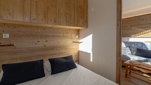 A bedroom with a wooden headboard, a bed with white bedding, and a view of another room with a patterned sofa. - Renovated apartment near slopes with wifi (Val Thorens)