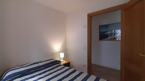 A bedroom with a bed, a bedside table with a lamp, and a door leading to another room.