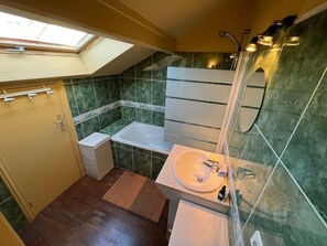 Un baño pequeño con tragaluz, bañera, lavamanos y espejo.