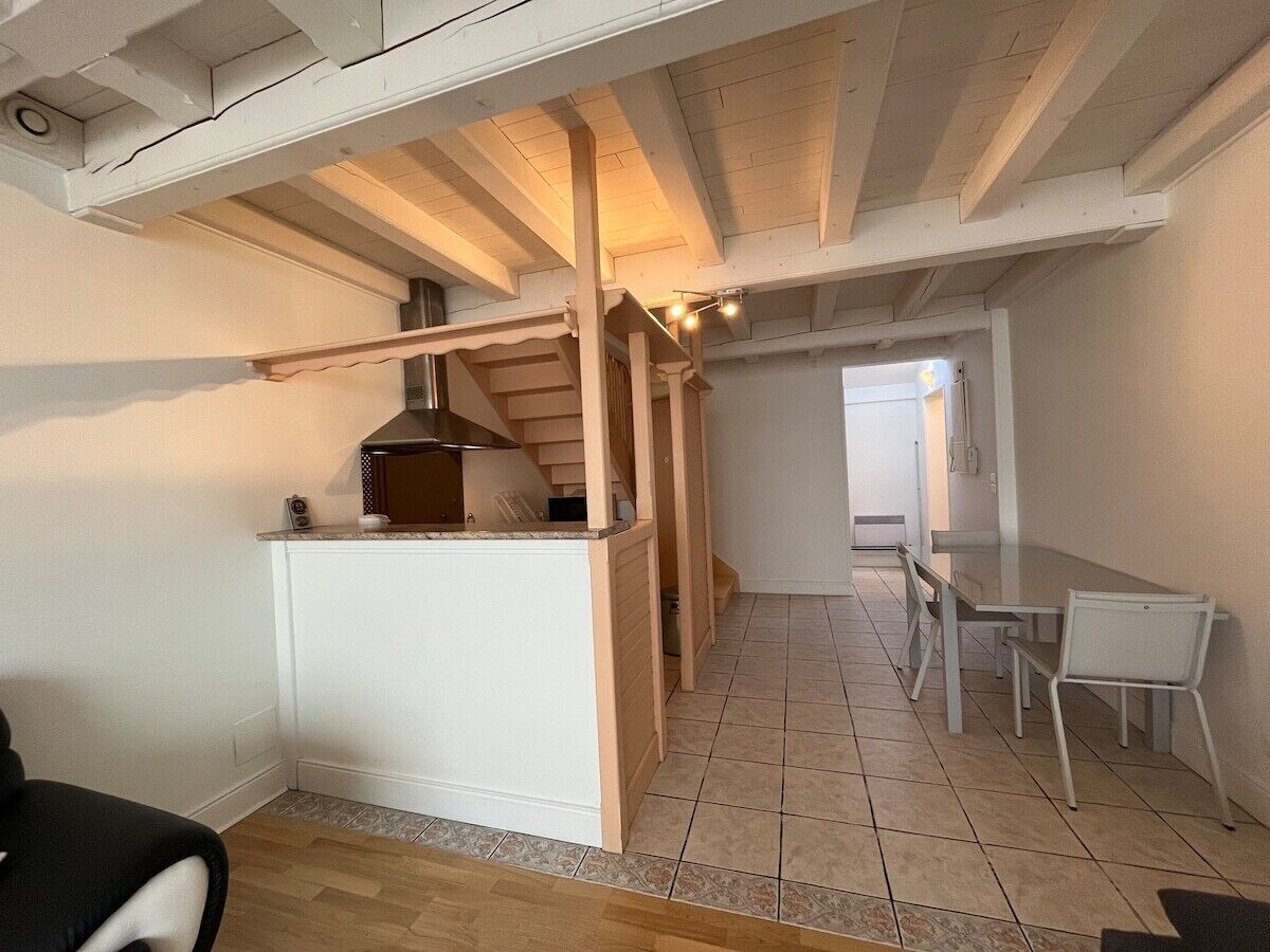 Cocina compacta con horno empotrado, comedor con mesa y sillas, y estructura de techo de madera.