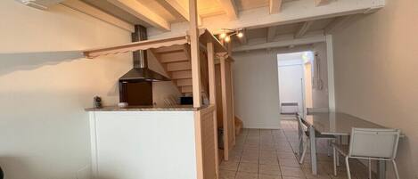 Cocina compacta con horno empotrado, comedor con mesa y sillas, y estructura de techo de madera.