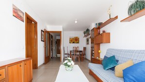 A living room with a sofa, coffee table, and a dining area with chairs and a table. - AirCon Apartment close to the Beach - UHC MAR Y LUZ (Salou)