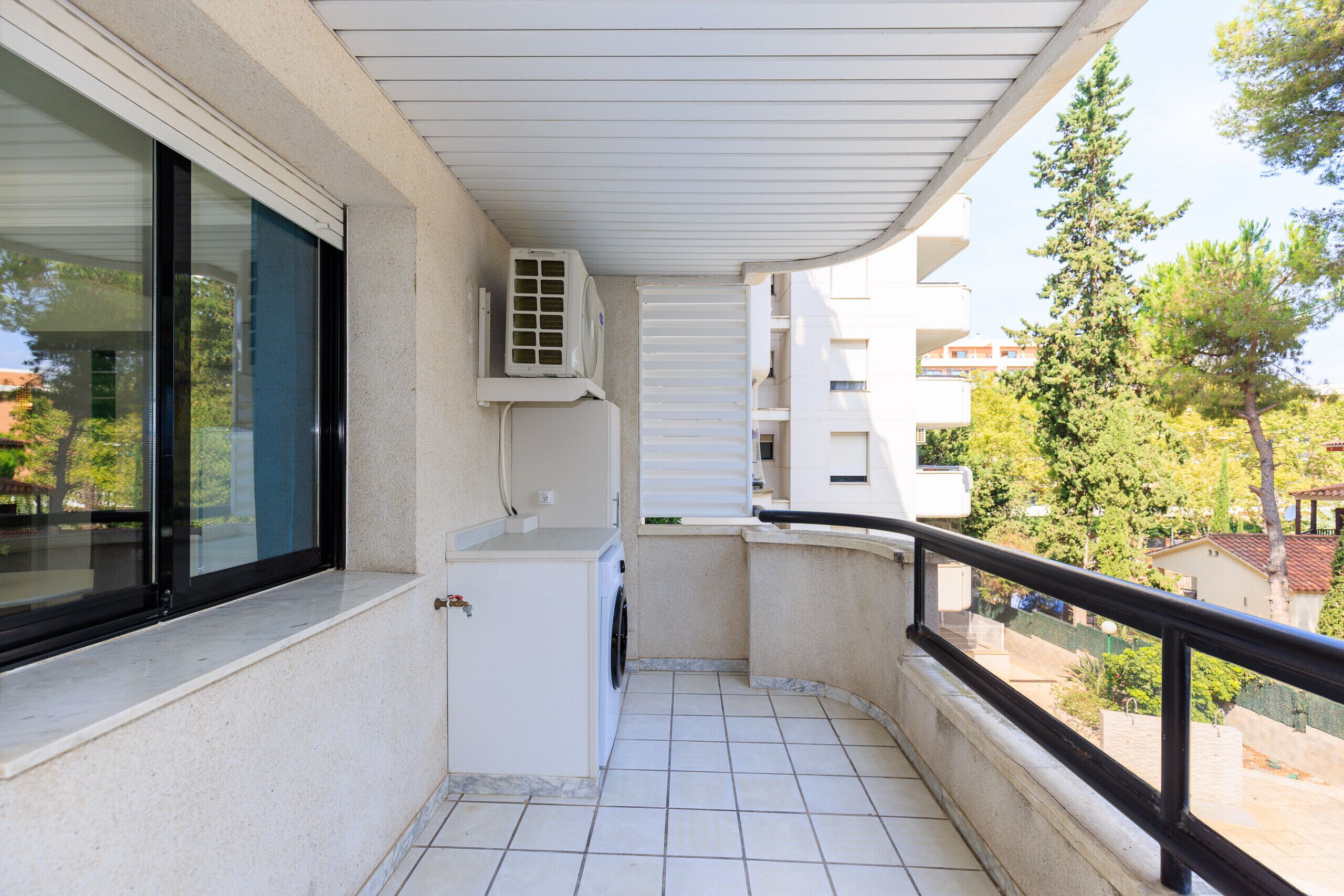 Un balcón con lavadora, ventana y unidad de aire acondicionado.