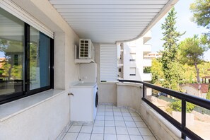 A balcony with a washing machine, a window, and an air conditioning unit.