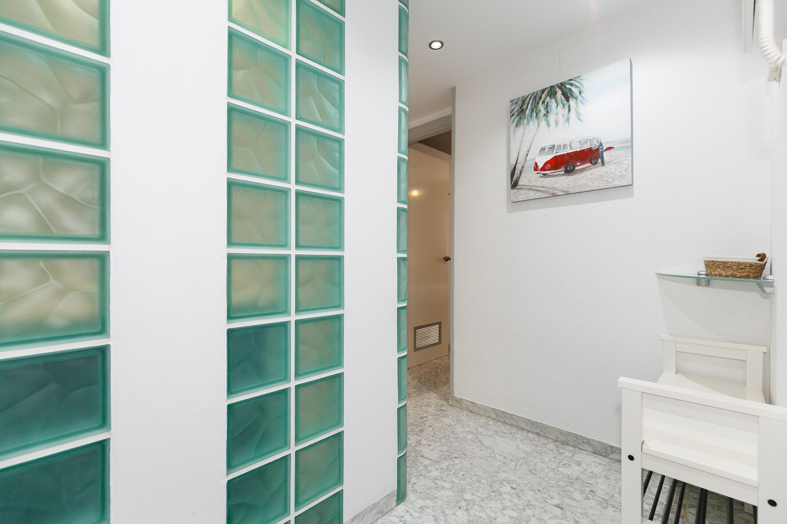 Un pasillo con un separador de vidrio, un banco blanco y una obra de arte en la pared que representa un autobús rojo.