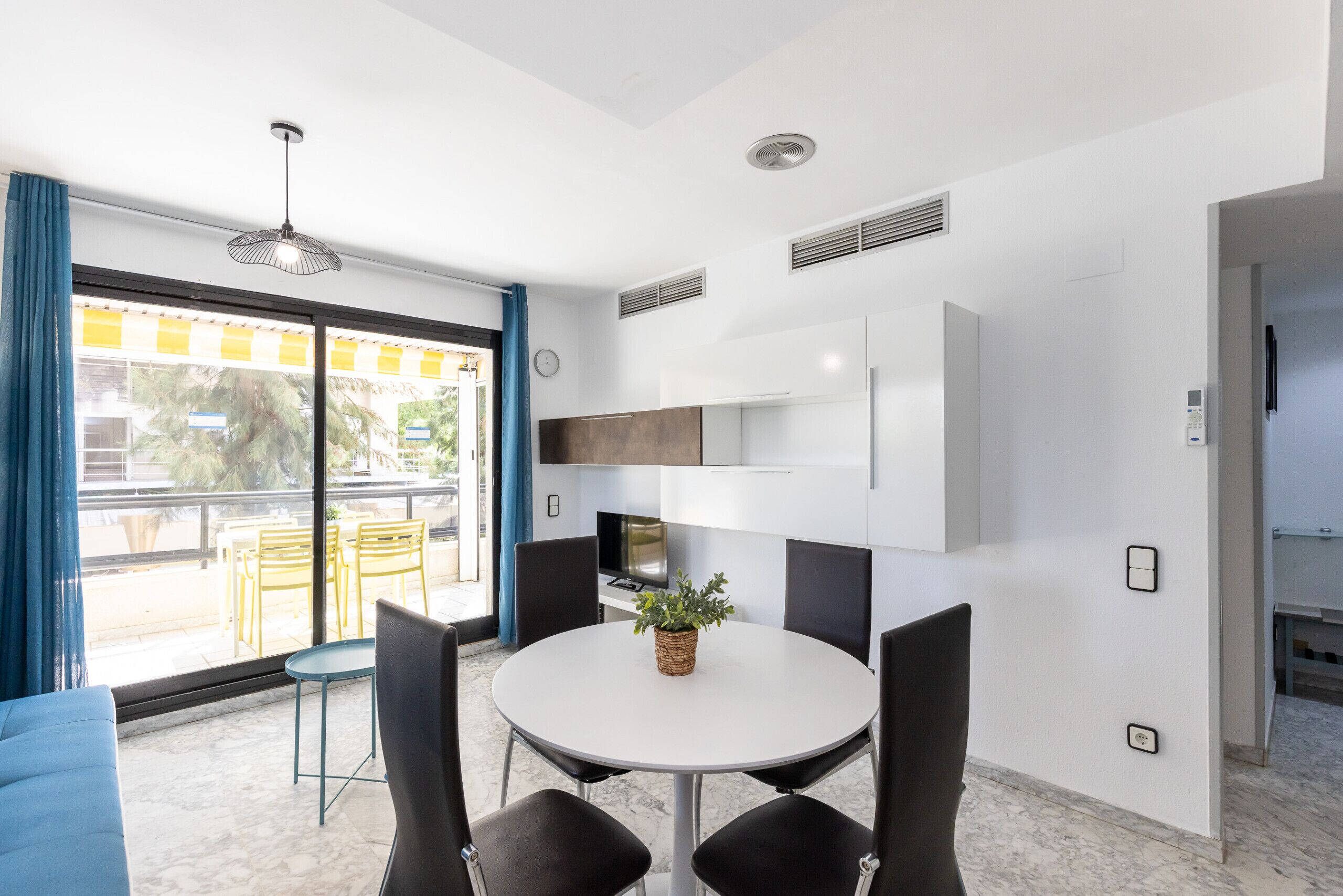 Una cocina moderna con armarios blancos, horno empotrado y comedor con mesa redonda y sillas.