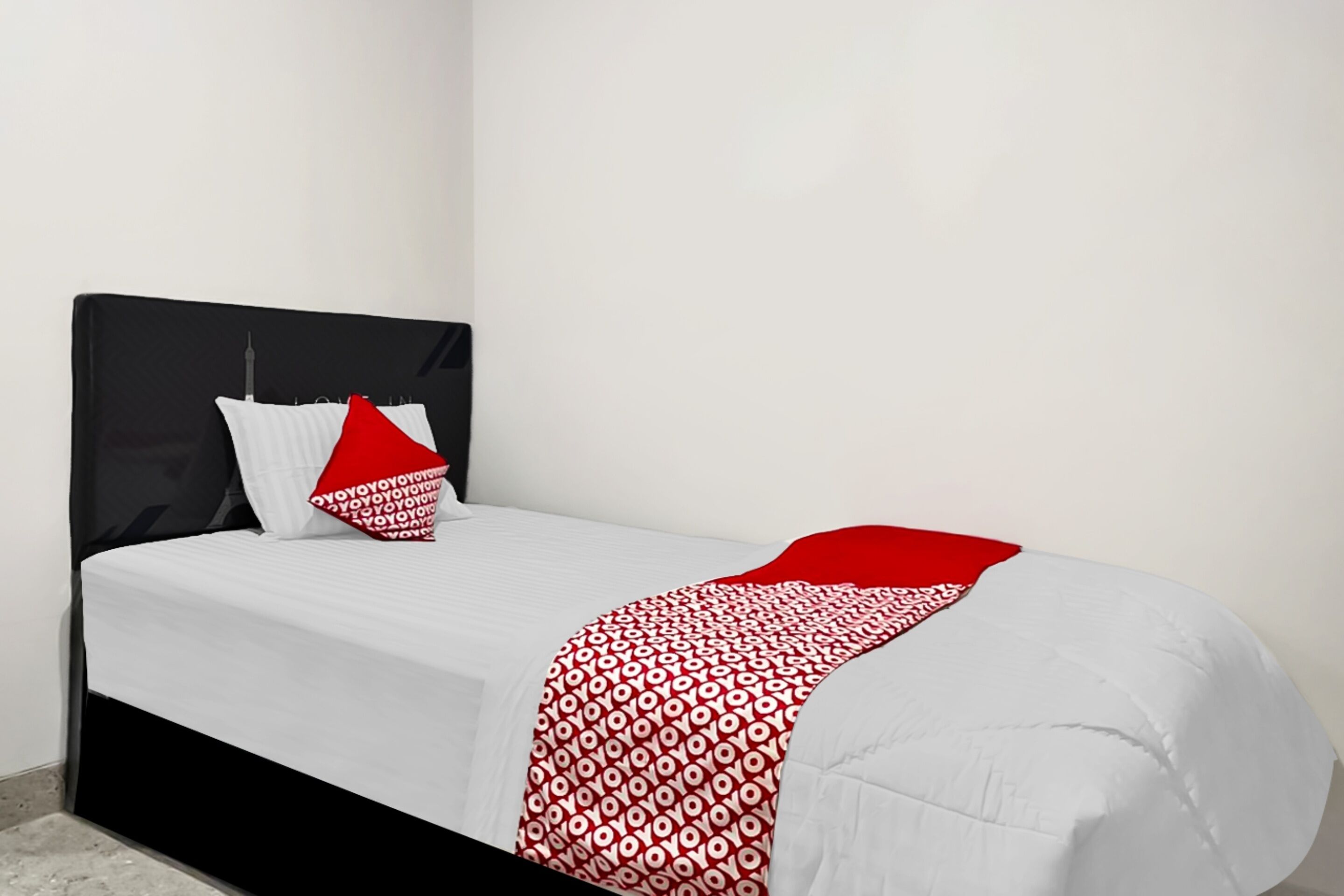 Una cama con cabecera negra, ropa de cama blanca y una manta con estampado rojo y blanco.