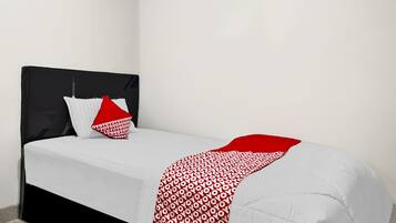 Una cama con cabecera negra, ropa de cama blanca y una manta con estampado rojo y blanco.