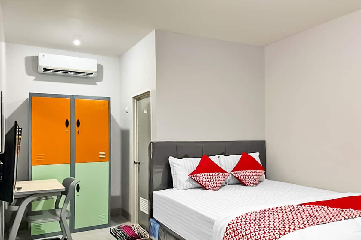 A hotel room with a bed, a desk, and an air conditioning unit.