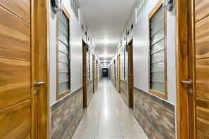 A long, narrow hallway with wooden doors and frosted glass windows, leading to a darkened room at the end. - Hotel O Kbr Home (Kelapa Dua)