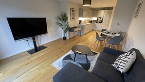Een moderne woonkamer met een flatscreen televisie, een grijze bank, een kleine ronde tafel en een potplant.