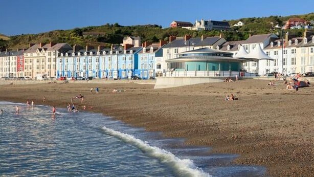 A beach with a row of colorful buildings, a sandy shore, and a few people in the water.