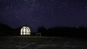 A starry night sky with a large, illuminated dome structure in the foreground.
