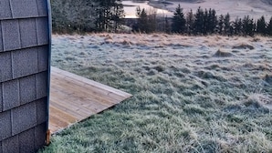 A rustic cabin with a wooden deck overlooking a frost-covered landscape and a valley.