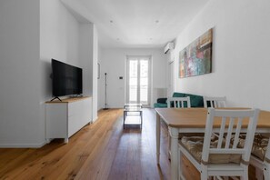 Un salón moderno con un televisor de pantalla plana, una mesa de comedor con sillas, un sofá y un cuadro en la pared.