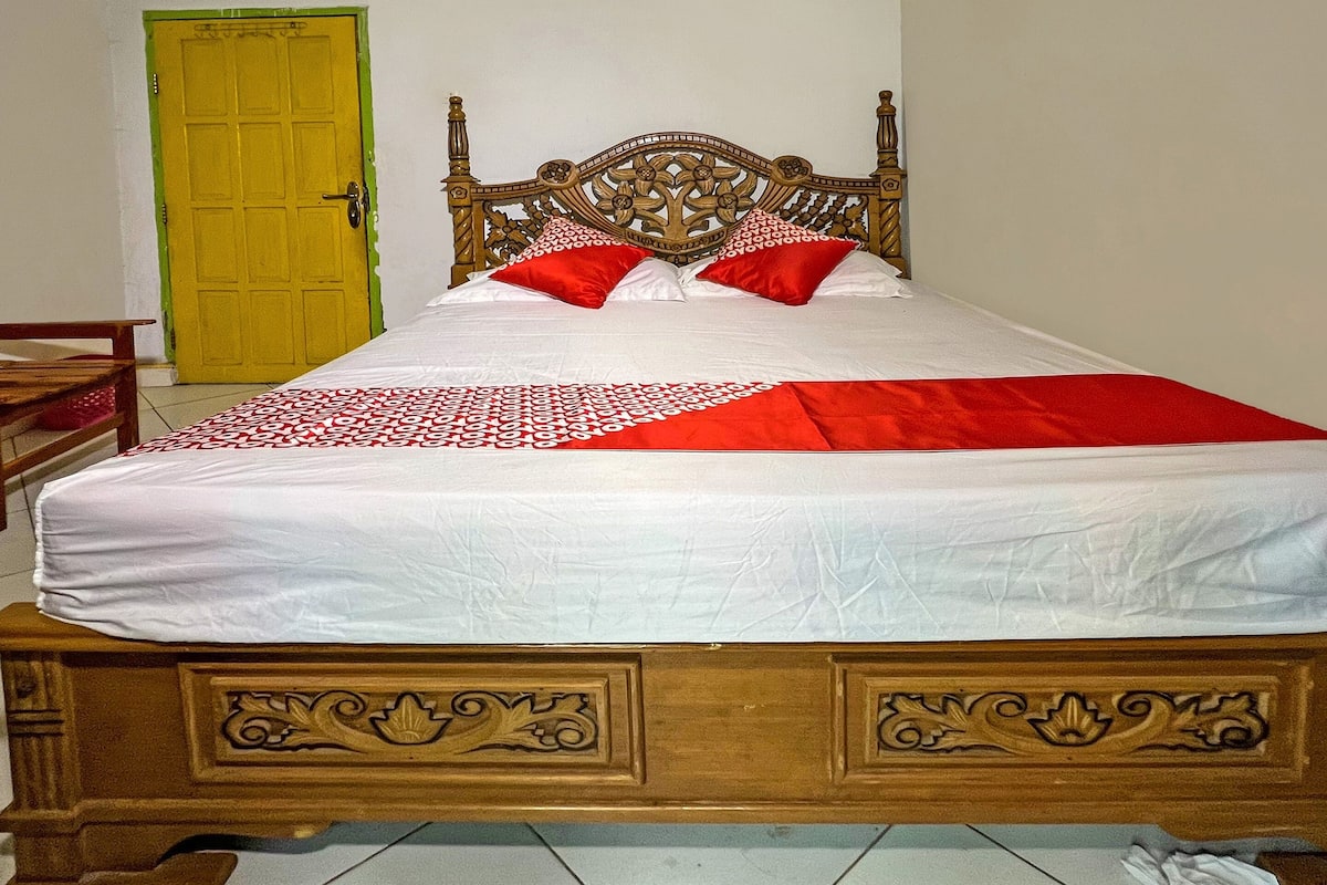 A bed with a wooden headboard, two red pillows, and a white bedspread.
