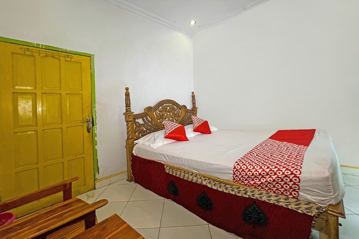 A room with a bed, a wooden bench, a yellow door, and a white wall.