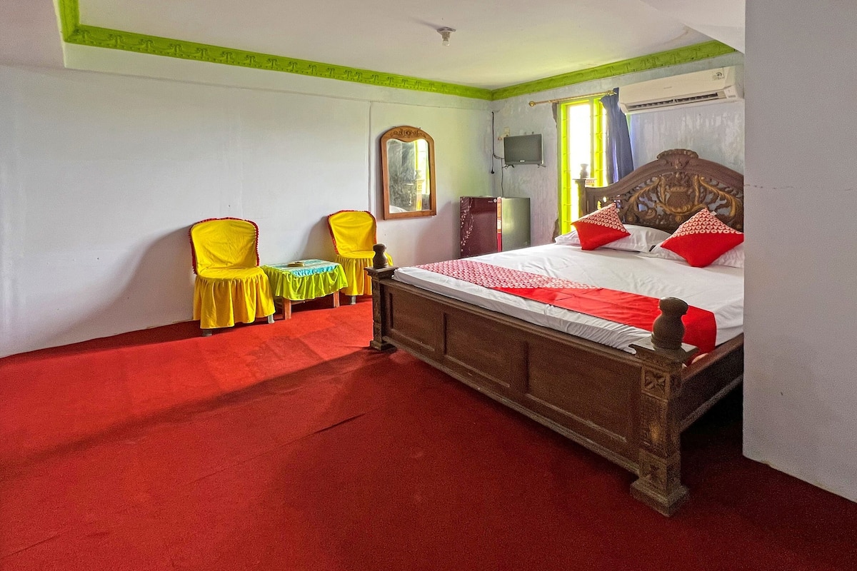 A bedroom with a wooden bed, a red carpet, a yellow chair, and a small table.