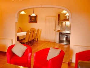A dining area with a table and chairs, a kitchen with a stove, and a red armchair.