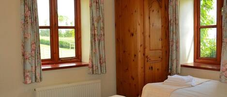 A room with two beds, a wooden wardrobe, and windows with floral curtains.
