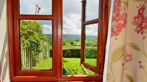 Ein Zimmer mit Holzboden, einem Fenster mit Blick auf eine grüne Landschaft und einem blumigen Vorhang.
