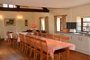 A dining area with a long table and chairs, a fireplace, and a kitchen with a sink and cabinets.