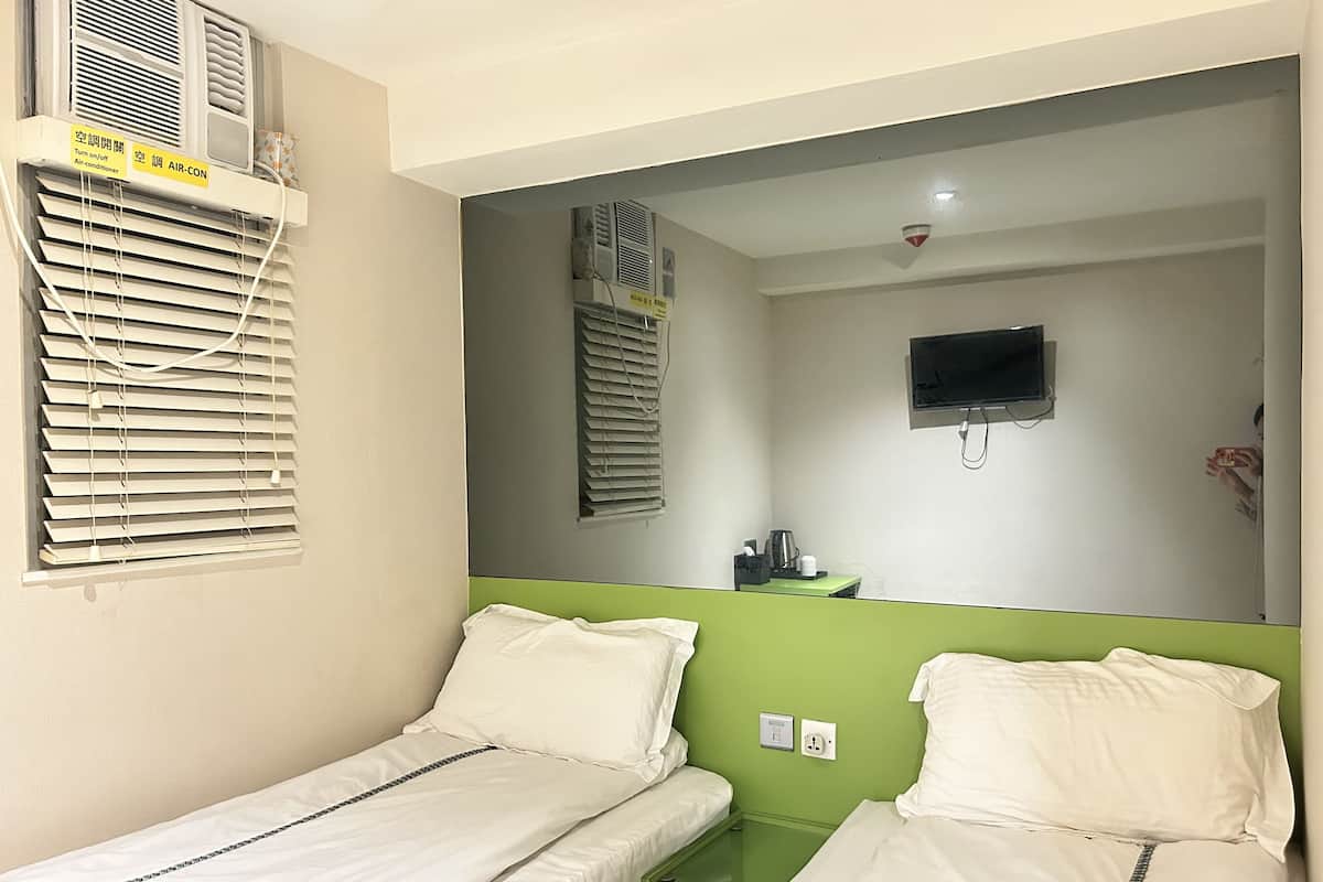Et værelse med to enkeltsenge, en grøn accentvæg, et ophængt TV og en aircondition med kontrolpanel.