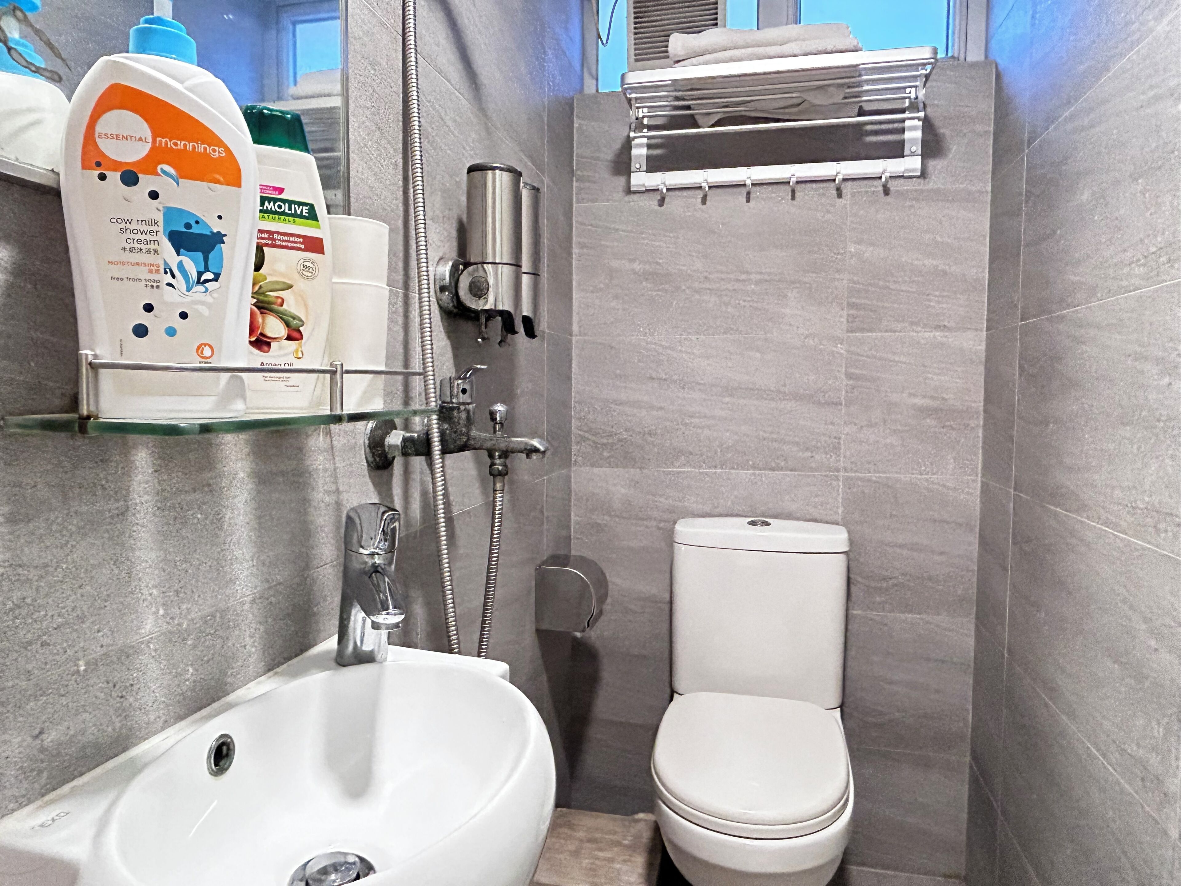 A bathroom with a white sink, toilet, and shower. There are toiletries on a shelf.