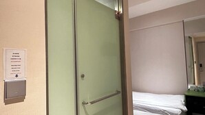 A hotel room with a green door, a bedside table with a lamp, and a bed with white bedding. - POP E INN (Kowloon)