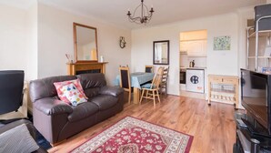 A living room with a brown leather sofa, a wooden dining table, and a kitchen area in the background. - Central 2BD Flat in Heart of Dublin (Dublin)