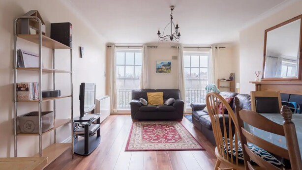 A spacious living area with a black leather sofa, a wooden dining table, and a bookshelf. - Central 2BD Flat in Heart of Dublin (Dublin)