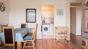 A compact living space with a dining table, chairs, a small kitchen with a washing machine, and a bookshelf. - Central 2BD Flat in Heart of Dublin (Dublin)