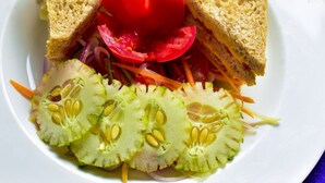 Un sándwich con rodajas de tomate y pepino sobre un plato blanco.
