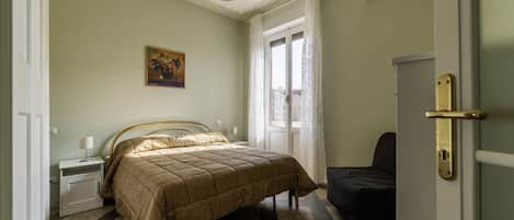 A bedroom with a bed, a nightstand, a chair, a door, and a window with curtains.