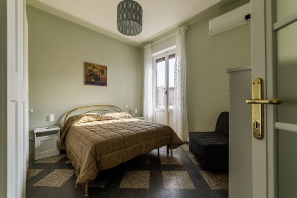 A bedroom with a bed, a nightstand, a chair, a door, and a window with curtains.