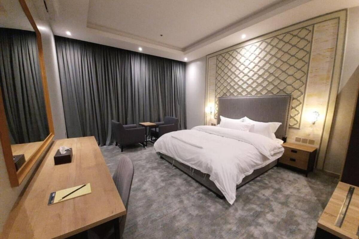 Une chambre d’hôtel comprenant un lit, un bureau, une chaise, une petite table et un mur orné d’un motif géométrique.