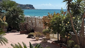 A courtyard with potted plants, a decorative fence, and a view of the sea. - Erika House (Bova Marina)