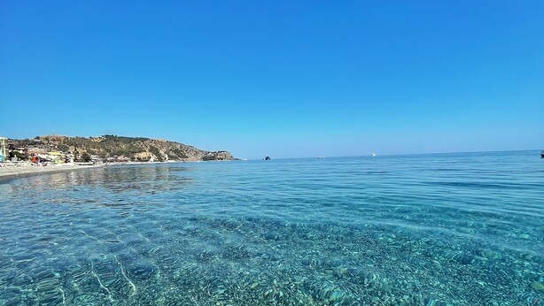 A clear view of a coastal beach with visible rocks and a distant shoreline. - Erika House (Bova Marina)