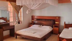 A bedroom with a wooden bed, bedside tables, a desk, and a window with curtains. - Maralink Hotel (Narok)