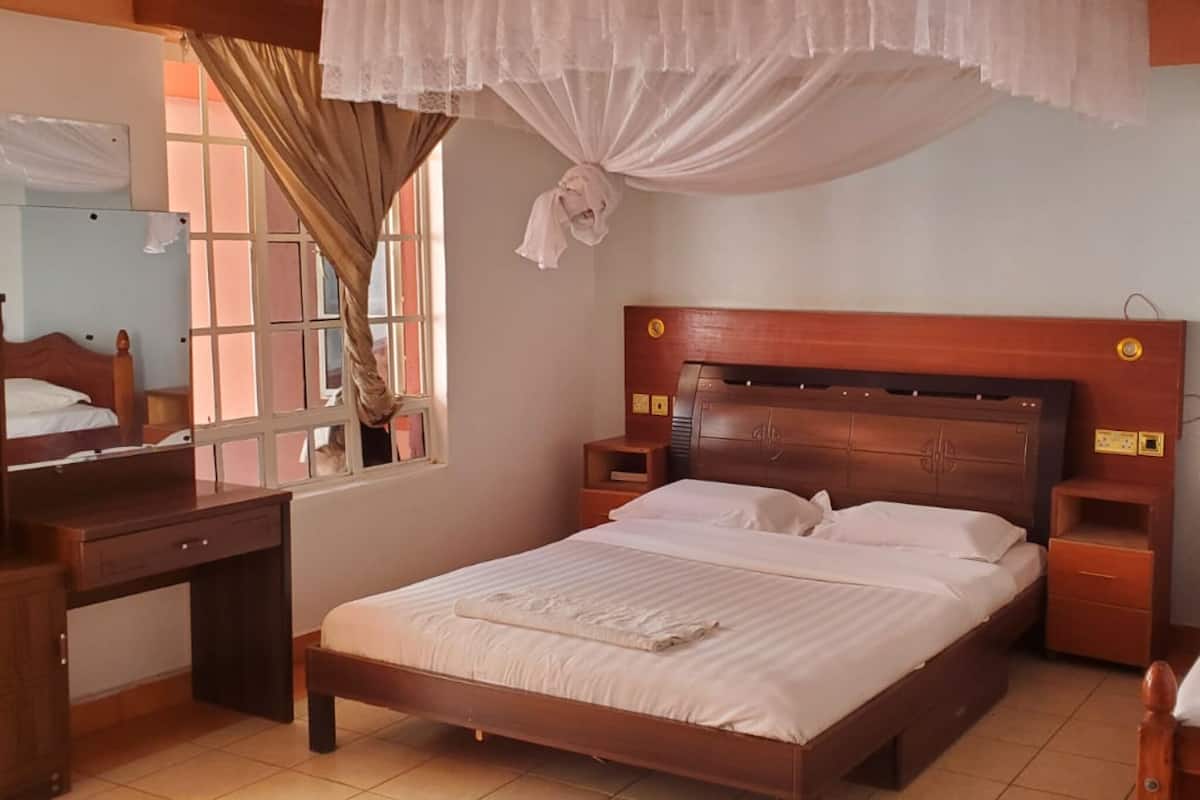 Quarto com cama de madeira, mesas de cabeceira, escrivaninha e janela com cortinas.