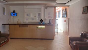 A reception area with a wooden desk labeled "RECEPTION," a television mounted on the wall, and a person standing behind the desk.