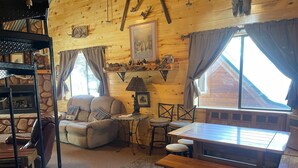 Een gezellig chaletinterieur met houten inrichting, een open haard, een bank, een eettafel en een bankje.