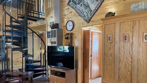 Een houten interieur met een wenteltrap, een televisie en een klok aan de muur.