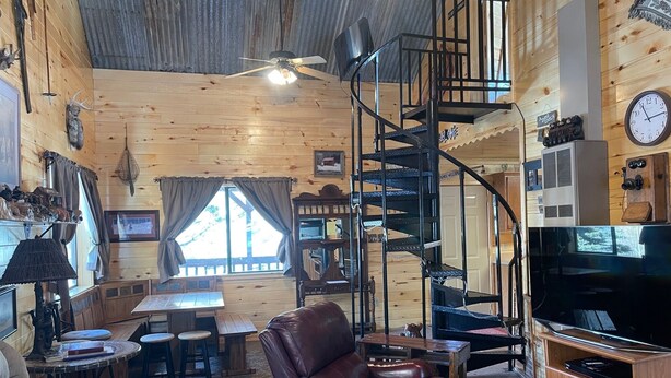 Een gezellig interieur van een chalet met een spiltrap, houten wanden, een leren bank, een eethoek en een televisie.