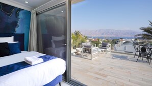 Ein modernes Hotelzimmer mit einem großen Bett, Blick auf die Stadt und Berge sowie einer Sitzgelegenheit im Freien.