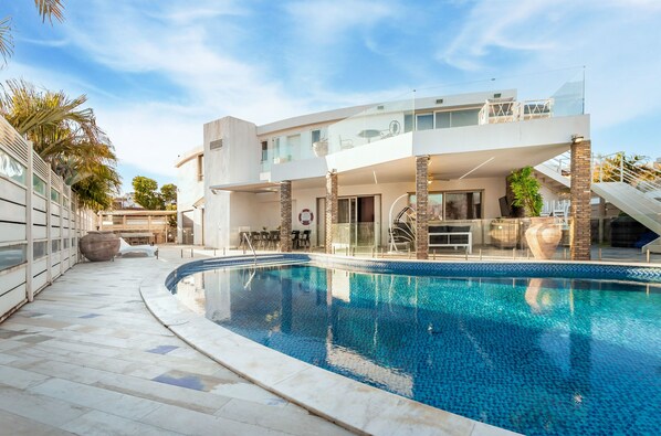 A modern house with a swimming pool, a covered patio, and a staircase leading to a balcony.